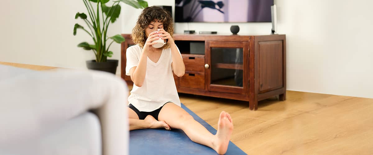 Frau trinkt Kaffee auf ihrer Yoga-Matte