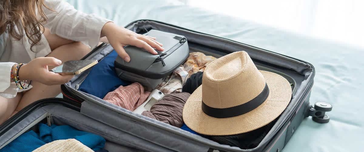 Kofferpacken mit Kleidung und Strohhut