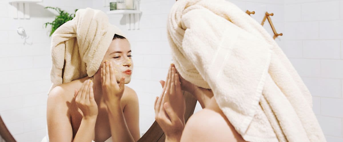 Mädchen mit Gesichtsmaske schaut in den Badezimmerspiegel