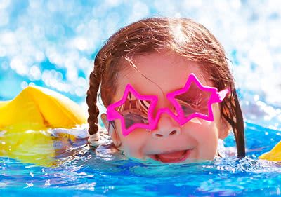 Kleinkind mit Schwimmflügel und Sonnenbrille im Wasser