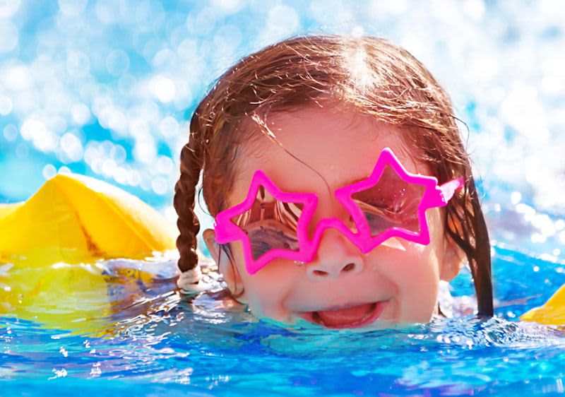 Kleinkind mit Schwimmflügel und Sonnenbrille im Wasser