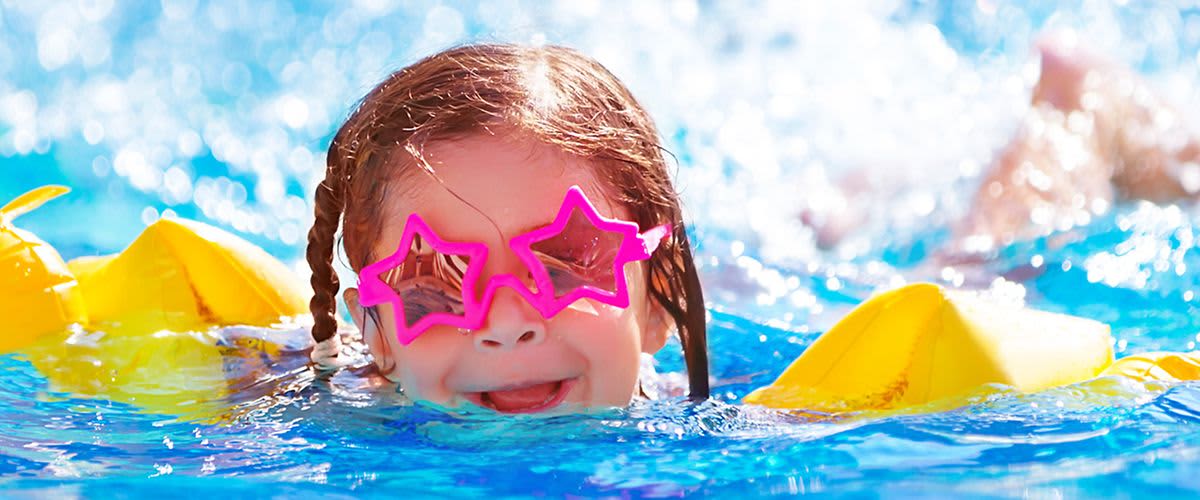 Kleinkind mit Schwimmflügel und Sonnenbrille im Wasser