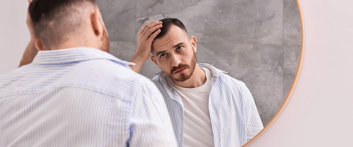 Mann betrachtet sich im Spiegel mit grauem Hintergrund