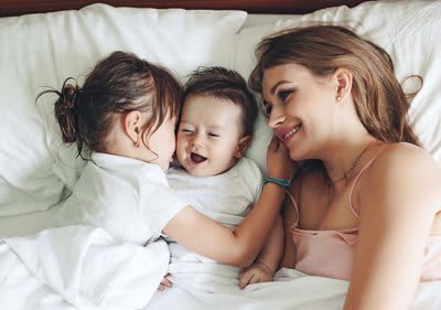 Mama liegt mit ihren Kindern im Bett