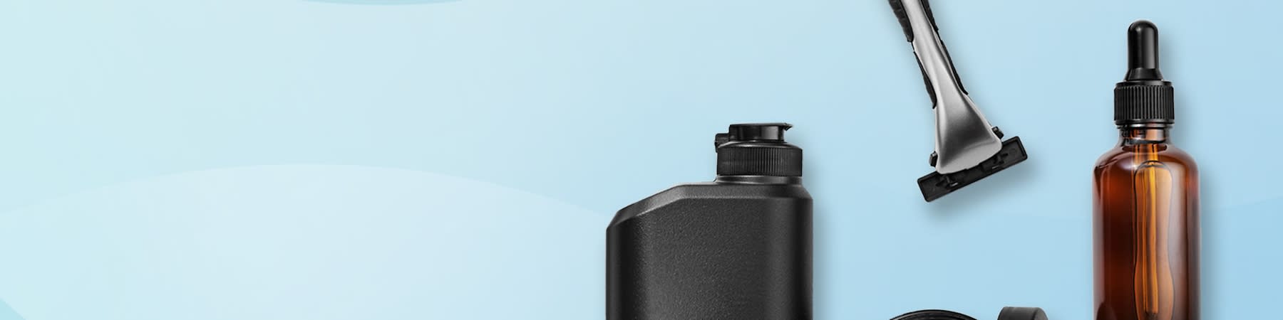 Ein Rasierer, eine schwarze Flasche, ein offener Tiegel und eine braune Tropfflasche auf blauem Hintergrund