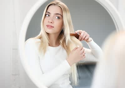 Frau kämmt blondes Haar vor einem Spiegel