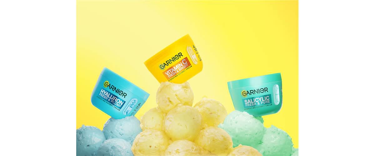 Drei Garnier-Gesichtspflege-Tiegel in Gelb, Türkis und Mint auf einem Haufen gelber, grüner und blauer Schaumbällchen, gut lesbare Marken- und Produktnamen sichtbar