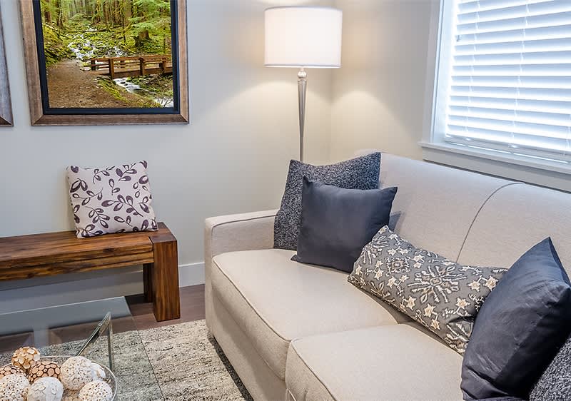 Wohnzimmer mit Sofa und Kissen neben Lampe und Fenster mit Bild an der Wand