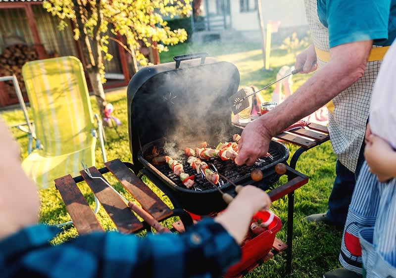 Grillen im Garten mit Fleischspießen auf dem Grill und Menschen beim Kochen