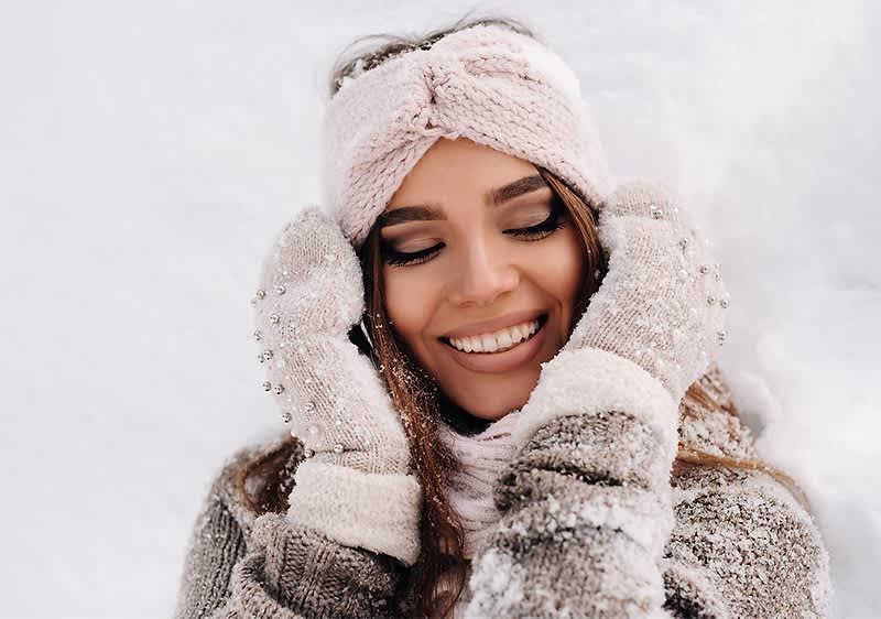 Frau in Winterkleidung im Schnee mit rosa Stirnband und Handschuhen