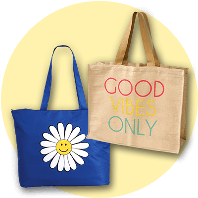 Zwei Einkaufstaschen vor einem hellgelben Hintergrund. Links eine blaue Tasche mit einer großen weißen Blume und einem gelben Smiley in der Mitte. Rechts eine beigefarbene Tasche mit der bunten Aufschrift „GOOD VIBES ONLY“