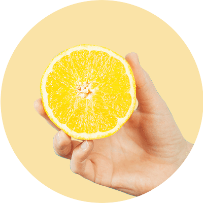 Eine Hand hält eine halbierte Orange vor einem hellgelben Hintergrund