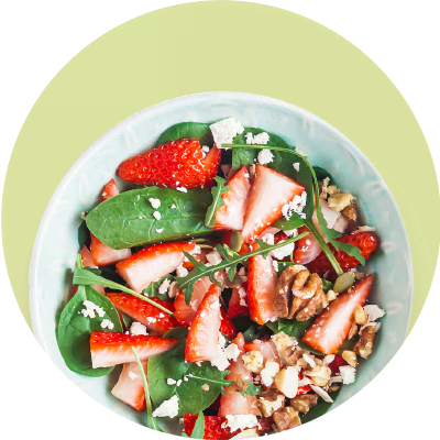 Ein Salat mit frischen Erdbeeren, Spinatblättern, Walnüssen und Feta in einer hellblauen Schüssel auf einem hellgrünen Hintergrund