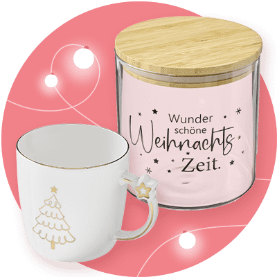 Eine weiße Tasse mit goldener Weihnachtsbaum-Verzierung und Stern am Henkel steht neben einem Glasbehälter mit Holzdeckel, der die Aufschrift „Wunder schöne Weihnachts Zeit“ trägt