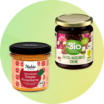 Zwei Produktgläser auf grünem Hintergrund. Links ein Glas von Nabio mit der Aufschrift „Getrocknete Tomate Pinienkerne“, rechts ein Glas von dmBio mit der Aufschrift „Dattel-Haselnuss Creme“