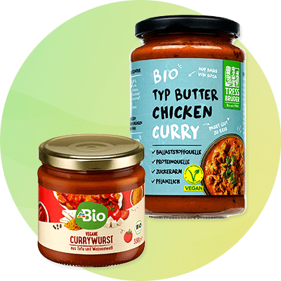 Zwei Gläser mit Bio-Lebensmitteln. Links ein Glas mit veganer Currywurst und rotem Etikett, rechts ein Glas mit Bio Typ Butter Chicken Curry und blauem Etikett. Beide Produkte sind vegan zertifiziert.