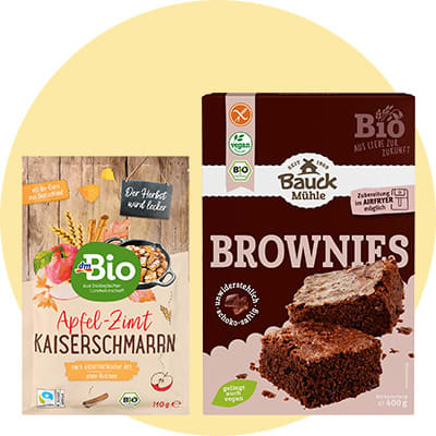 Zwei Bio-Backmischungen nebeneinander: links dmBio „Apfel-Zimt Kaiserschmarrn“ in beige Verpackung mit Holzoptik und Bild von Kaiserschmarrn, rechts Bauck Mühle „Brownies“ in brauner Packung mit Bild von zwei Schokokuchenstücken
