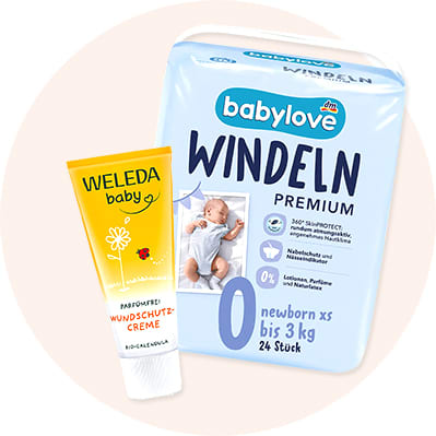 Eine gelbe Tube Weleda Baby Wundschutzcreme mit rotem Schriftzug neben einer Packung Babylove Windeln Premium für Neugeborene bis 3 kg mit der Aufschrift „0 newborn xs bis 3 kg 24 Stück“