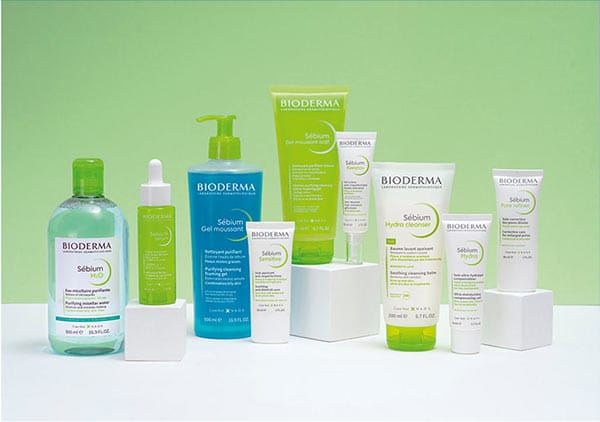 Mehrere Bioderma Sébium Produkte auf weißen Podesten vor einem grünen Hintergrund, darunter Flaschen und Tuben mit grünen und weißen Etiketten