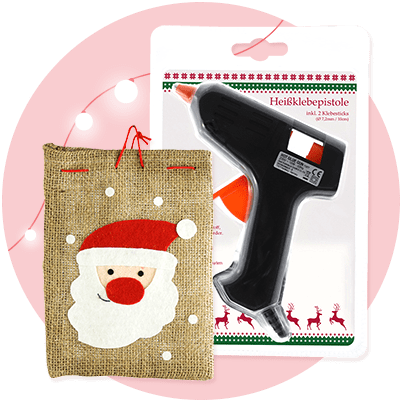 Eine schwarze Heißklebepistole auf einer Verpackung mit der Aufschrift „Heißklebepistole inkl. 2 Klebesticks“, daneben ein Jutesack mit einem weißen und roten Weihnachtsmann-Gesicht aus Filz