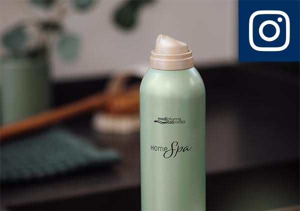 Eine grüne Sprühflasche mit der Aufschrift „medipharma cosmetics Home Spa“ steht auf einem dunklen Tisch. Im Hintergrund sind verschwommene grüne Pflanzen zu sehen