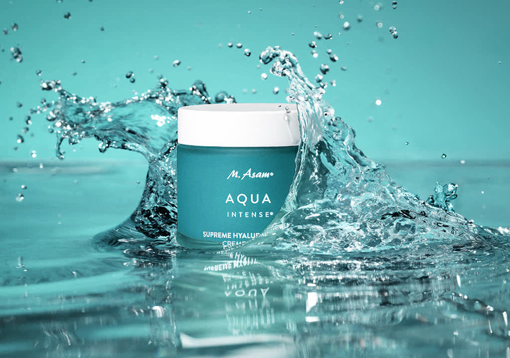 Eine türkisfarbene Creme-Dose mit der Aufschrift „M. Asam Aqua Intense Supreme Hyaluron Cream“ steht in spritzendem Wasser