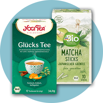 Verpackungen von zwei Teesorten: Links eine grüne Packung von Yogi Tea mit der Aufschrift „Glücks Tee“ und einer Abbildung einer Teetasse mit Zimt und Orangenschale. Rechts eine Packung von dmBio mit der Aufschrift „Matcha Sticks“ und einer Illustration von grünen Teeblättern und einer Teeschale.