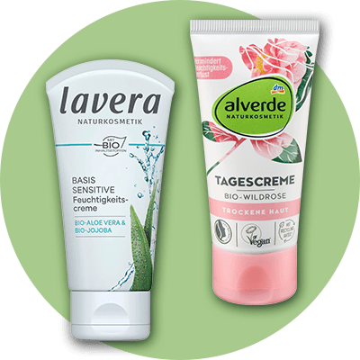 Zwei Tuben Naturkosmetik: Links eine weiße Tube von Lavera mit der Aufschrift „Basis Sensitive Feuchtigkeitscreme Bio-Aloe Vera & Bio-Jojoba“, rechts eine rosa-weiße Tube von Alverde mit der Aufschrift „Tagescreme Bio-Wildrose Trockene Haut“ und dem dm-Logo.