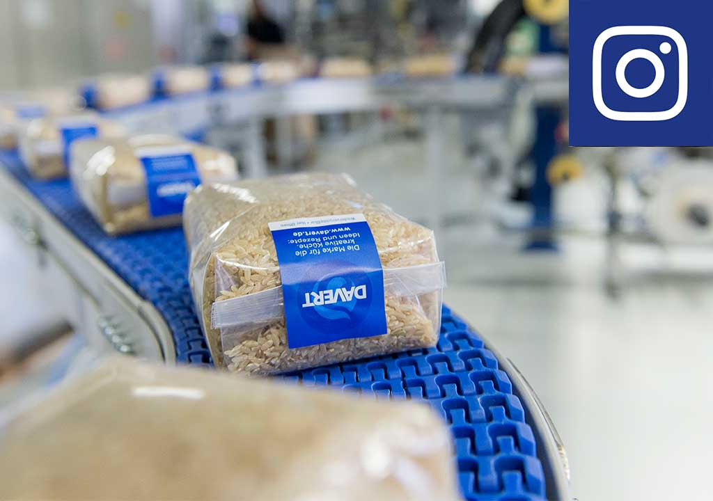 Mehrere Personen tragen orangefarbene Blumengirlanden und haben die Hände zum Gebet gefaltet. Im Hintergrund sind Bäume und weitere Menschen zu sehen.