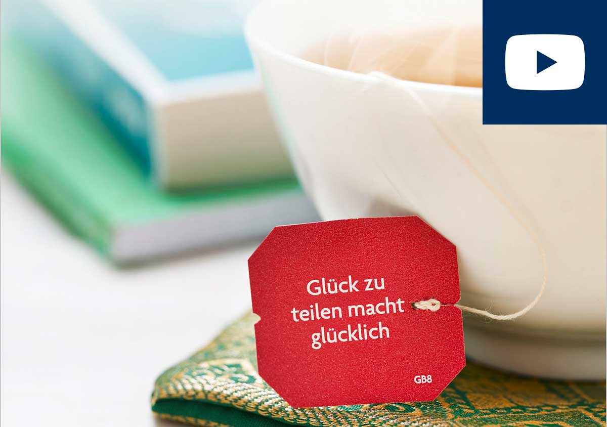 Eine Teetsse mit Teebeutel-Etikett "Glück zu teilen macht glücklich" und YouTube Logo Ikon rechts