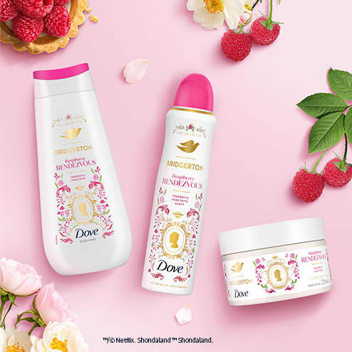 Eine Produktverpackungskollektion von Dove mit der Aufschrift „Bridgerton Raspberry Rendezvous“. Links eine weiße Flasche mit pinkem Deckel, in der Mitte ein Spray mit pinkem Deckel, rechts ein weißer Tiegel. Dekoriert mit Himbeeren und Blumen.