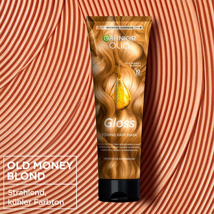 Eine Garnier Olia Haarmaske mit der Aufschrift „Gloss Toning Hair Mask“ und „Old Money Blonde“ auf einer Verpackung mit goldenen Haarsträhnen. Im Hintergrund sind geschwungene Linien in einem ähnlichen Farbton zu sehen.
