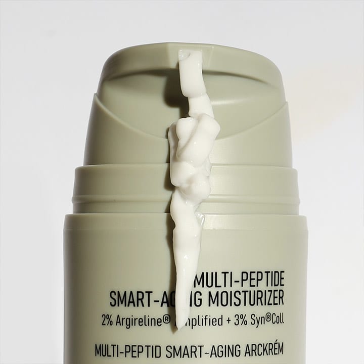 Eine graue Flasche mit der Aufschrift „Multi-Peptide Smart-Aging Moisturizer“, aus der weiße Creme herausfließt