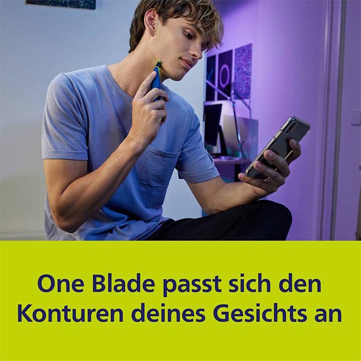 Ein Mann in einem blauen T-Shirt hält einen Rasierer an sein Gesicht und schaut auf ein Smartphone. Darunter steht der Text: „One Blade passt sich den Konturen deines Gesichts an“