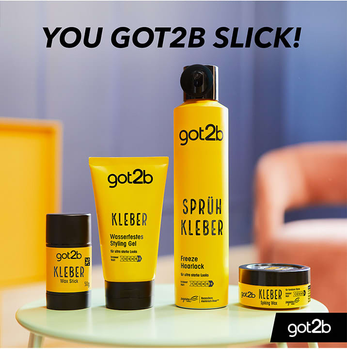 Vier gelbe Stylingprodukte der Marke got2b mit schwarzer Schrift, darunter ein Sprühkleber in hoher Dose, ein Wasserfestes Styling Gel in Tube, ein Wax-Stick und ein kleines Döschen Haarwachs, vor unscharfem Hintergrund