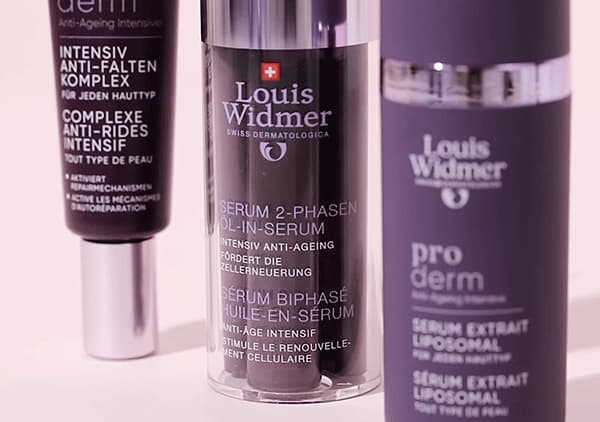 Drei Spenderflakons von Hautpflegeprodukten der Marke Louis Widmer, mittig ein Zylinder mit der Aufschrift „SERUM 2-PHASEN OIL-IN-SERUM“, links und rechts je ein weiterer dunkler Pumpspender mit ergänzenden Produkttexten wie „pro derm“ und „Intensiv Anti-Falten Komplex“