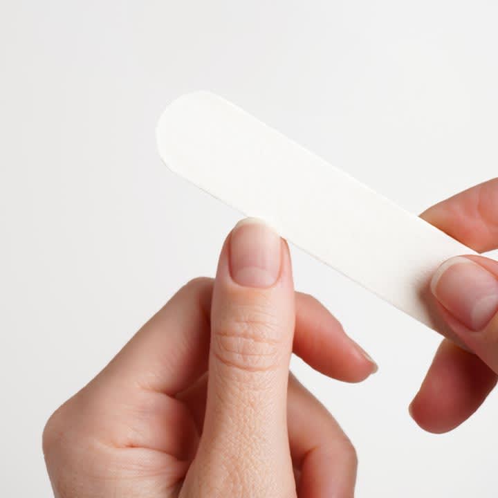 Zwei HĂ€nde halten eine weiĂe Nagelfeile und feilen an einem kurzen Fingernagel