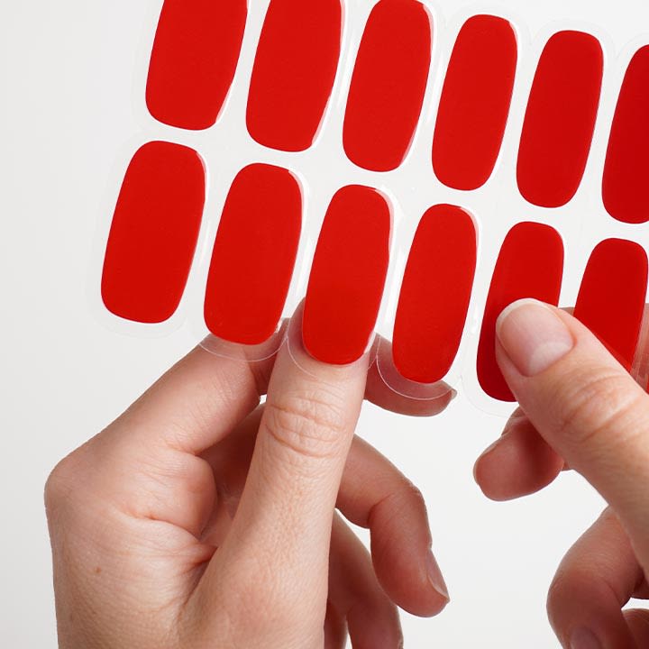 HÀnde bringen rote Selbstklebende Nailsticker von einer TrÀgerfolie auf einen Finger an