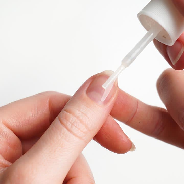 Hand, die mit einem kleinen Pinsel NagelpflegeflĂŒssigkeit auf einen Fingernagel auftrĂ€gt