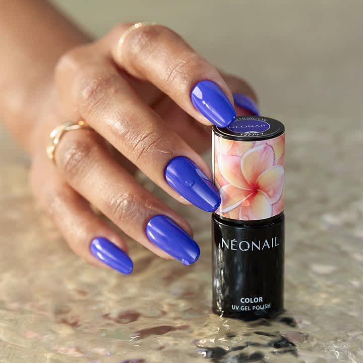 Hand mit fünf glänzend lackierten, violett-blauen Fingernägeln hält eine schwarze Nagellack-Flasche der Marke NEONAIL mit floral bedrucktem Deckel