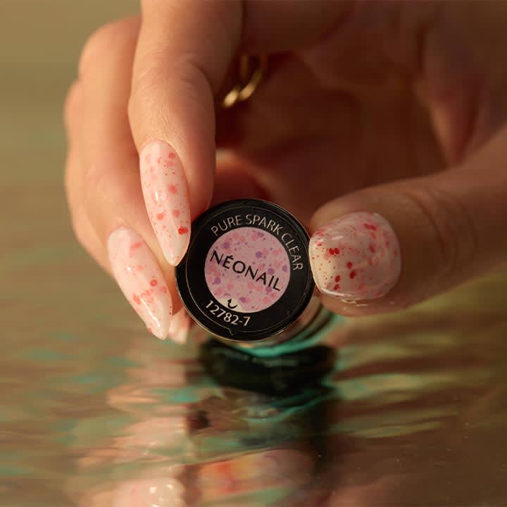 Hand mit roséfarbenen, gesprenkelten langem Nageldesign hält ein rundes Nail-Produktdöschen mit Aufschrift „NEONAIL“ und „PURE SPARK CLEAR“
