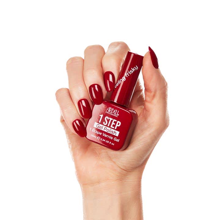 Hand hält rote Nagellack-Flasche der Marke Ardell mit der Aufschrift „1 STEP Gel Polish“, Fingernägel lackiert in passendem dunklem Rot