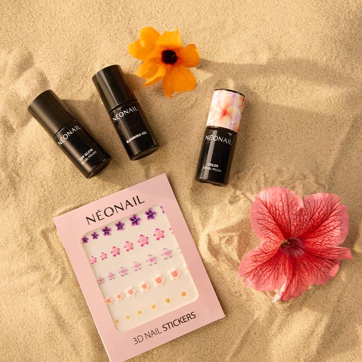 Vier schwarze Nagelpflege-Flaschen mit Marke „NEONAIL“, eine rosafarbene Packung „NEONAIL 3D NAIL STICKERS“ mit kleinen Blumenaufklebern auf Sand gelegen, dazu zwei orange-rosa Blüten
