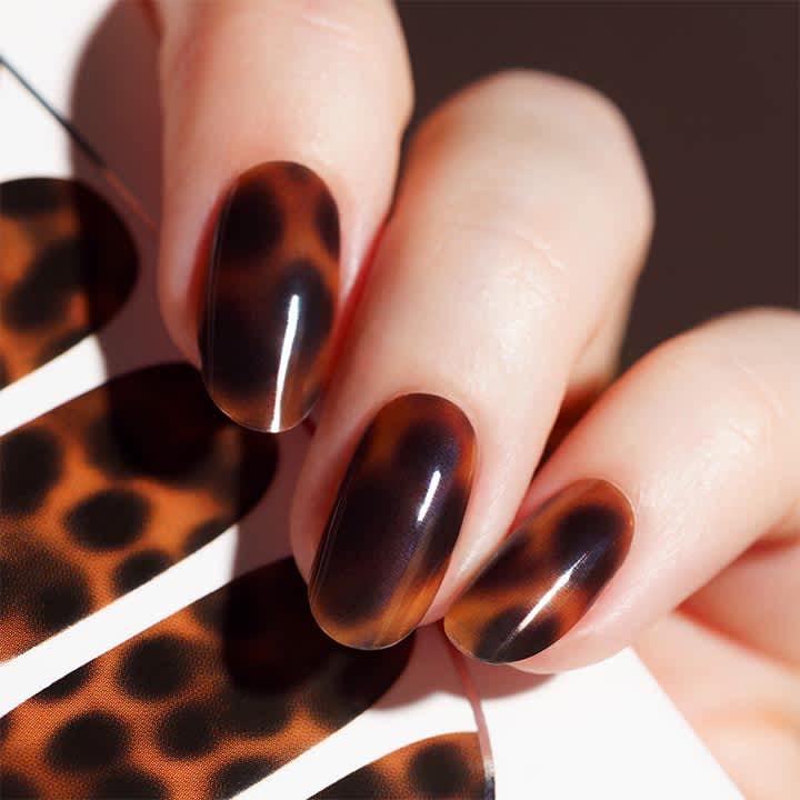 Vier ovale Fingernägel mit glänzendem, braun-schwarzem Schildpatt-Nageldesign auf hellhäutigen Fingern, daneben ein Schildpatt-Muster als Hintergrundfragment