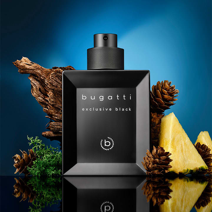 Schwarze quadratische Parfumflasche mit Sprühkopf, Aufschrift „bugatti exclusive black“, umgeben von Tannenzapfen, Holzstück, grüner Moospflanze und Ananasstücken