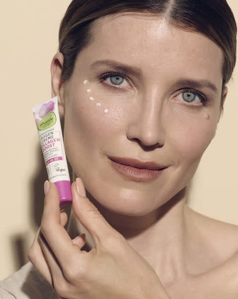 Frau hält eine pink-weiße Tubenverpackung der Marke alverde mit der Aufschrift „Augencreme Collagen Boost“, kleine Tupfen der Creme sind neben ihrem rechten Auge aufgetragen