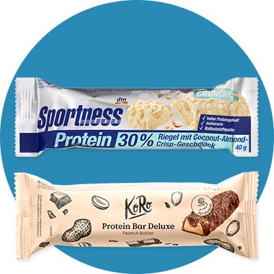 Zwei proteinreiche Riegel: oben ein blauer Sportness Protein Riegel 30% mit Aufschrift „Riegel mit Coconut-Almond-Crisp-Geschmack“ und 40 g, unten ein heller KoRo Protein Bar Deluxe mit Aufschrift „Peanut butter“ und Abbildung eines aufgeschnittenen Riegels