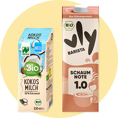 Zwei Getränkepackungen vor grünem Kreis: links dmBio Kokosmilch 250 ml, rechts Vly Barista Haferdrink „Schaumnote 1.0“ in Tetra Pak