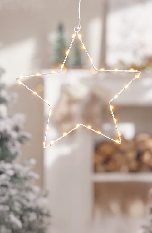 Drahtstern mit kleinen warmweißen Lichterketten, hängend vor unscharfem Weihnachtsdekor. Bild mithilfe von KI erstellt