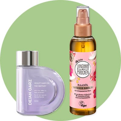 Zwei Haarpflegeprodukte vor grünem Kreis: links halbmondförmige lila Flasche mit silbernem Verschluss und Aufschrift „DEJAN GARZ VIOLET HAIR OIL“, rechts durchsichtige Pumpspray-Flasche mit goldener Flüssigkeit und rosa Etikett „ANGHAAR MÄDCHEN HAARÖL INTENSE REPAIR“